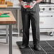 A man in a Uncommon Chef black customizable classic chef pants holding a bowl of food in a professional kitchen.