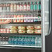 A woman reaching into the Beverage-Air VueMax air curtain merchandiser for a drink.