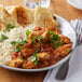 A white plate of chicken curry with a knife and fork on a table.