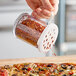 A hand using a Carlisle polycarbonate shaker to sprinkle spices on a pizza.
