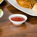 A white American Metalcraft porcelain sauce cup filled with red sauce on a table.