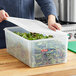 A person using an Araven translucent plastic food pan with airtight lid to fill it with green leaves from a salad bar.