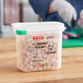 A person wearing gloves cuts chickpeas in a white Araven plastic container.