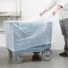 A person putting a plastic bag on a Cambro dish cart.