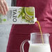 A person pouring Tazo Green Tea Matcha Latte concentrate into a glass pitcher.