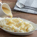 A person pouring Knorr low sodium chicken gravy into a bowl of mashed potatoes.