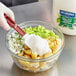 A gloved hand mixing Hellmann's Vegan Mayonnaise in a bowl.