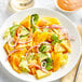 A white plate of salad with mango and pineapple on a table.