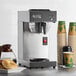 An Avantco silver and black automatic coffee maker on a counter with coffee cups.