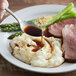 A plate of mashed potatoes and meat with LeGout Au Jus gravy served on a table with a spoon.