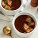 Two bowls of brown French onion soup with bread in them.