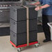 A man pushing a stack of black Cambro Cam GoBox pan carriers on a black Compact Camdolly.