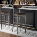 Two Lancaster Table & Seating Boomerang bar stools with brown vinyl seats and backs at a bar counter.