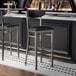 A Lancaster Table & Seating clear coat bar stool with black vinyl seat and back at a black counter.