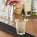 A person pouring a drink into a Duralex glass filled with ice and lime on a bar.