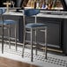 Two Lancaster Table & Seating navy vinyl bar stools with a clear coat finish at a black bar counter.