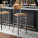 Two Lancaster Table & Seating bar stools with light brown vinyl seats and backs at a bar counter.