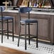 A black bar stool with a navy vinyl seat and backrest, positioned at a bar counter.