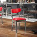 A metal chair with a clear coat finish featuring a red vinyl seat and backrest.