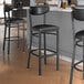 Three black Lancaster Table & Seating Boomerang Series bar stools with black vinyl seats and backs sitting in front of a counter.