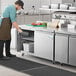 An apron-wearing man standing in front of an Avantco worktop freezer.