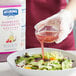 A person pouring Hellmann's Raspberry Vinaigrette into a bowl of salad.