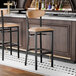 A black metal bar stool with a light brown vinyl seat and backrest.