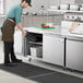 A man in a kitchen apron opening an Avantco undercounter freezer.