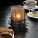A Hollowick Craftsman black low iron candle holder with a lit candle next to a plate of coffee and cookies.