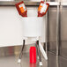 A white Prince Castle Ketchup Collector filled with ketchup bottles on a stainless steel counter.