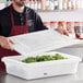 A man holding a Vigor white polyethylene food storage box lid on a container of food.