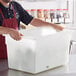 A man wearing a red apron holding a white Vigor plastic food storage container.