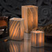 Three white Alabaster candle holders on a table with lit candles inside.