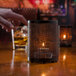 A Chantilly black and copper perforated metal Hollowick candle holder on a table with a lit candle.