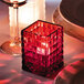 A red glass cube candle holder on a table with a lit candle inside.