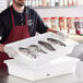 A man holding a white Vigor polyethylene food container filled with fish on ice.