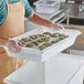 A man using a white Vigor food drain box to hold a tray of food.