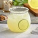 A clear plastic stemless fish bowl glass filled with a yellow beverage, garnished with a lime slice and a salted rim.