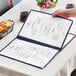 A hand holding a blue menu open on a table.