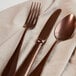 A Sola vintage copper dessert spoon on a white cloth with a fork and knife.