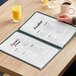 A hand holding a H. Risch TED deluxe menu on a table.