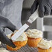 A person wearing black gloves uses a Dexter-Russell offset spatula to frost a cupcake.