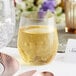 A Visions clear plastic stemless wine glass filled with yellow liquid on a table with a place setting at a catering event.