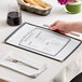 A hand holding a black H. Risch, Inc. menu on a table.