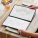 A person opening a black rectangular menu with gold corners.