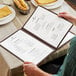 A man holding a TEDD menu cover at a table with bread and a glass.