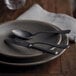 A plate with a Sola Baguette Vintage stonewash stainless steel spoon and fork on it.