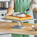 A person in a kitchen using an Ateco aluminum cake stand to cut a cake.