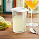 An Anchor Hocking glass measuring cup with white liquid and a spoon next to a kiwi.