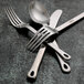 A Oneida Cooper stainless steel bouillon spoon on a table with a fork, knife, and other spoon.